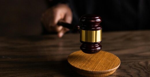 A close-up photograph of a wooden judge's gavel resting on a sounding block on a dark wooden table, representing the legal system and judicial rulings.